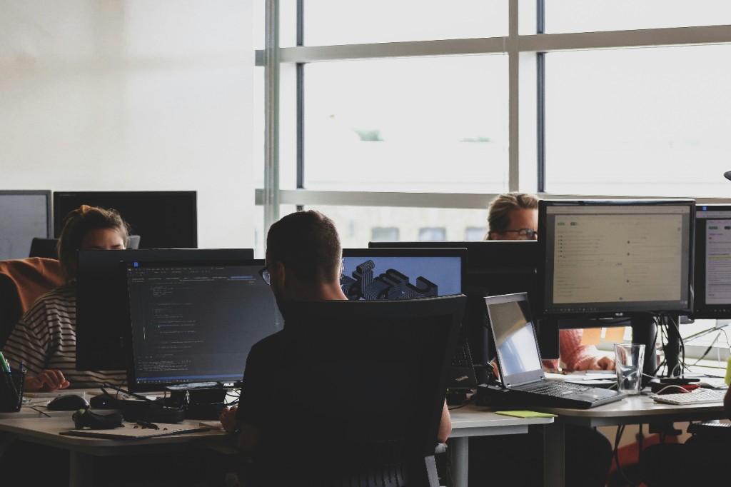 Engineering team collaborating at desks with multiple monitors in a bright office